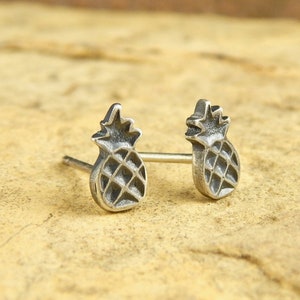 May include: A pair of silver pineapple stud earrings. The earrings are small and delicate, and they feature a detailed pineapple design.