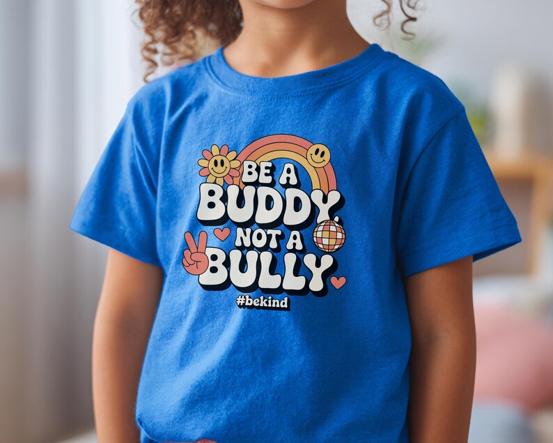 May include: A blue t-shirt with the text "BE A BUDDY NOT A BULLY" in a retro font, with a rainbow, smiley faces, and peace sign graphic. The hashtag #bekind is also included.
