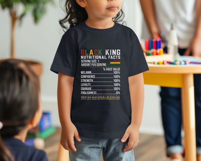 May include: A navy blue t-shirt with the text "BLACK KING NUTRITIONAL FACTS" and a list of values including Melanin, Confidence, Strength, Loyalty, Courage, and Foolishness. The shirt is worn by a child.