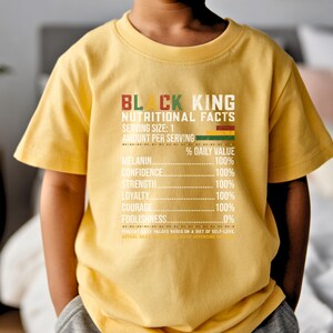 May include: A yellow t-shirt with the text "BLACK KING NUTRITIONAL FACTS" in red, green, and white. The shirt lists nutritional values for melanin, confidence, strength, loyalty, courage, and foolishness.
