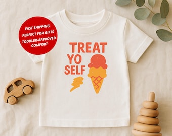 May include: White toddler t-shirt featuring the text "TREAT YO SELF" in orange, accompanied by an ice cream cone graphic. A wooden toy car and a wooden stacking toy are visible.