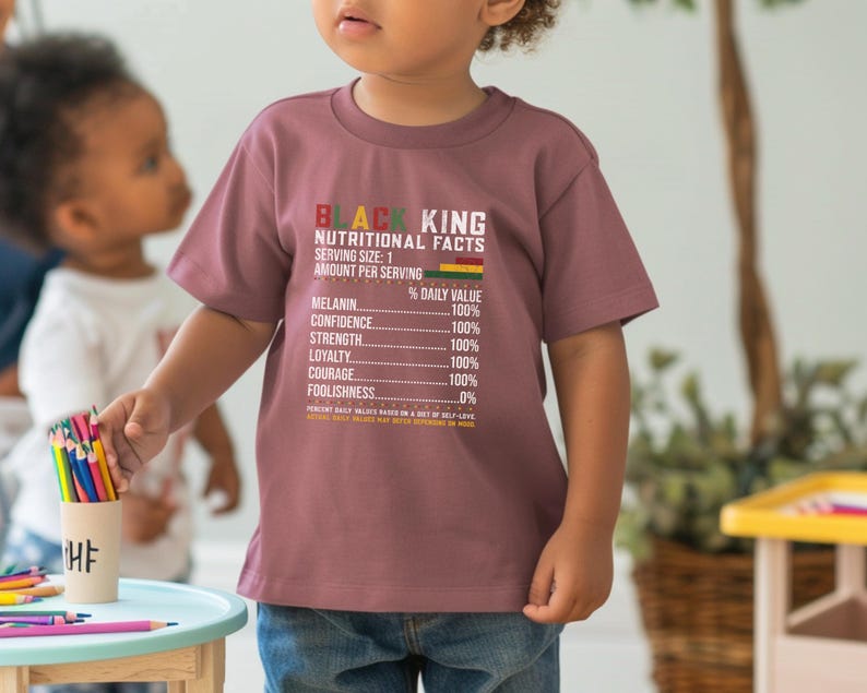 May include: A mauve-colored t-shirt with the text "BLACK KING NUTRITIONAL FACTS" printed on the front. The shirt features a nutritional facts label with percentages for melanin, confidence, strength, loyalty, and courage. A child is wearing the shirt.