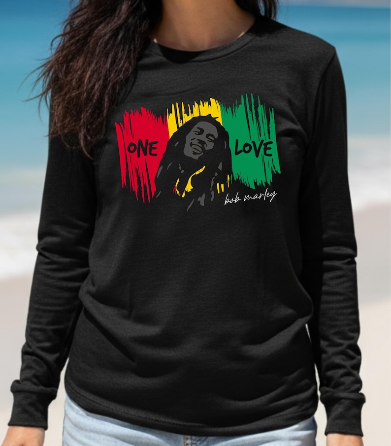 May include: Black long-sleeve shirt featuring a graphic of Bob Marley with the words "ONE LOVE" in red, yellow, and green brushstrokes. The shirt also includes the signature "bob marley" in white script.