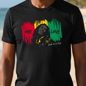 May include: Black t-shirt featuring a graphic of Bob Marley with the words "ONE LOVE" in red, yellow, and green. The design includes a portrait of Bob Marley and his signature.