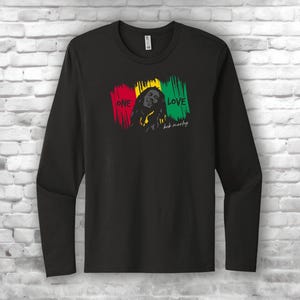 May include: Black long-sleeve shirt featuring a graphic of Bob Marley with the words "ONE LOVE" in red, yellow, and green. The shirt has a crew neck and is made of a soft material.