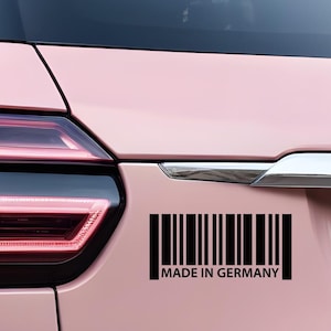 Peut inclure: Arrière d'une voiture rose avec un autocollant code-barres noir et blanc indiquant "MADE IN GERMANY". Le feu arrière de la voiture est rouge et noir.
