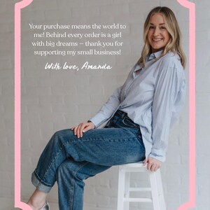 May include: A woman in a blue striped shirt and jeans sits on a white stool. The image is framed with a pink border and includes the text: "Your purchase means the world to me!" and "With love, Amanda."