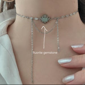 Puede incluir: Collar gargantilla plateado con un colgante central en forma de flor con una piedra de fluorita verde claro. Cadenas colgantes a&ntilde;aden un efecto de capas. El collar se lleva alrededor del cuello.