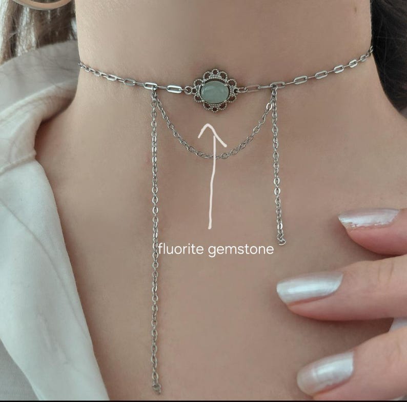 Puede incluir: Collar gargantilla plateado con un colgante central en forma de flor con una piedra de fluorita verde claro. Cadenas colgantes a&ntilde;aden un efecto de capas. El collar se lleva alrededor del cuello.