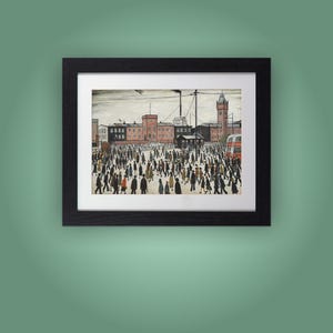 May include: Framed print showing a busy street scene. The artwork features a large crowd of people walking in front of buildings and a red double-decker bus. The buildings are brick-coloured, and the sky is overcast. The frame is black.