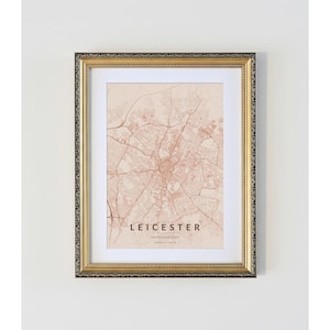 May include: A framed map print of Leicester, UK, in a neutral colour scheme. The map shows detailed street layouts and is enclosed in a gold-coloured frame with a decorative border. The city name is displayed in a serif font.