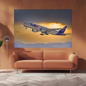 May include: A large canvas print of a FedEx cargo plane taking off against a dramatic sunset. The plane is white with purple and red accents. The print hangs above a peach-colored sofa in a modern living room setting.