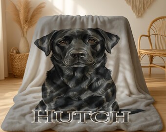 May include: A plush, light gray blanket featuring a detailed watercolor portrait of a black Labrador Retriever. The dog's name, "HUTCH", is displayed in a silver, block-style font at the bottom of the blanket. The blanket is draped over a surface.