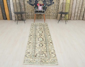 Könnte beinhalten: Ein hellbeiger Läuferteppich mit einem verblassten Blumenmuster. Der Teppich hat ein hellgrünes und braunes Design in der Mitte und einen hellbeigen Rand.