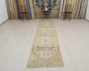 May include: A beige runner rug with a faded floral pattern. The rug has a distressed look and is made of a soft, woven material.