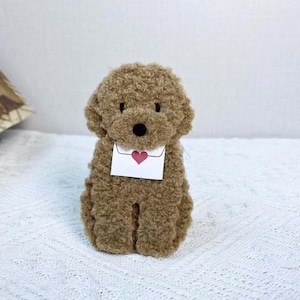 May include: A brown plush toy poodle holding a white envelope with a red heart on it.