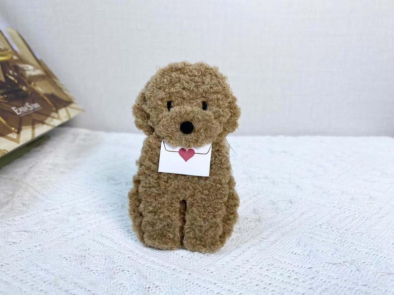 May include: A brown plush toy poodle holding a white envelope with a red heart on it.
