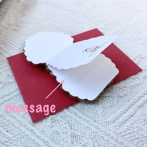 May include: A white card with a red envelope. The card is folded in half and has a scalloped edge. The envelope has the words "message" written on it.