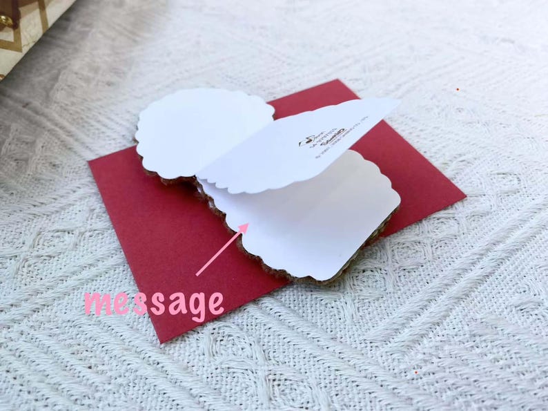 May include: A white card with a red envelope. The card is folded in half and has a scalloped edge. The envelope has the words "message" written on it.