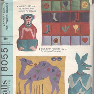 May include: A sewing pattern for children's room accessories. The pattern includes a monkey bag, put-away pockets, a pin-a-tail game, and a kanga-bag. The pattern is printed on a blue and white background.