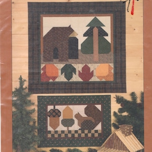 Puede incluir: Dos patrones de acolchado, "Bear Country" y "Greener Pastures", se muestran sobre un fondo de veta de madera. El primer patrón presenta un oso, un árbol y una casa con un borde de hojas rojas, naranjas y verdes. El segundo patrón presenta una ardilla, un árbol y una bellota con un borde a cuadros blanco y negro.