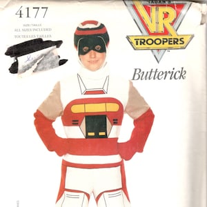 May include: A red, white and black costume for a child. The costume features a helmet with a black visor, a red and white torso with a black and yellow design, and white trousers with black and red accents. The costume is labelled "4177 Kaitlin Star" and is a "VR Troopers" costume.