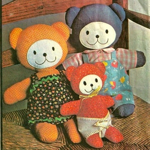May include: Three handmade teddy bears with white faces and smiling mouths. The bears are wearing different outfits: an orange bear in a floral dress, a blue bear in overalls, and a red bear in a diaper. The bears are made of fabric and have stitched details.