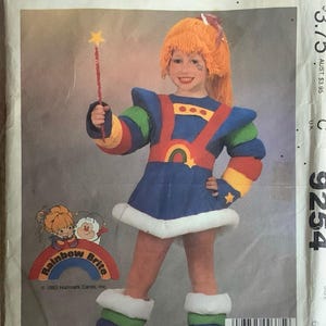 Op de afbeelding: Een naaipatroon voor een Rainbow Brite kostuum. Het patroon is voor een kinderkostuum en bevat een jurk, leggings en een hoofdband. Het patroon is van McCall's en het patroonnummer is 9254.