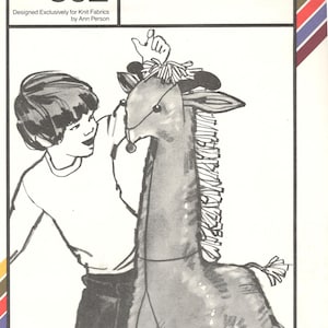May include: A black and white illustration of a child holding a stuffed giraffe toy. The giraffe has a long neck with a fringe of hair and a long tail. The toy is designed to be made from knit fabric. The pattern is titled "giraffe" and has the number 802 on it.