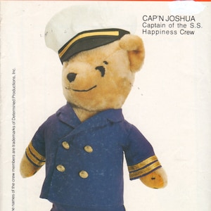May include: A teddy bear dressed as a captain, wearing a blue uniform with gold buttons and a white sailor hat with a gold band. The bear is labeled "Cap'n Joshua, Captain of the S.S. Happiness Crew".