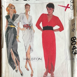 Könnte beinhalten: Ein Vintage-Schnittmusterumschlag von McCall's, Nummer 8043, mit Illustrationen von drei Varianten eines Wickelkleides von Halston. Die Entwürfe umfassen ein schwarzes Kleid mit goldenem Gürtel, ein weißes Kleid mit rotem Gürtel und ein rotes Kleid mit schwarzem Gürtel.