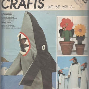 Op de afbeelding: McCall's Crafts naaipatroon met kostuumontwerpen. De afbeelding toont een haaienkostuum, bloemenkostuums en pinguïnkostuums. Het patroon bevat maten voor volwassenen en kinderen. De tekst "COSTUMES..." en "RAVESTIS..." is zichtbaar.