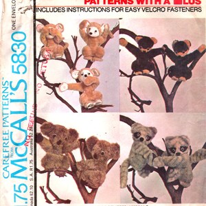 Può includere: Una busta di cartamodello McCall's vintage con istruzioni per realizzare un set di animali di peluche. L'immagine mostra vari animali di peluche, tra cui orsi, koala e procioni, appollaiati su rami di alberi. Il testo recita "PATTERNS WITH A PLUS".