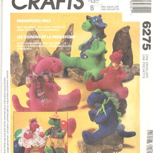 Op de afbeelding: McCall's Crafts patroon 6275 met pluche dinosaurus speelgoed. De omslag toont verschillende kleurrijke dinosaurussen in verschillende poses, waaronder groen, rood en blauw. De tekst luidt "Prehistoric Pals" en "Les Copains de la Préhistoire".