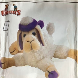 Op de afbeelding: Een Simplicity crafts/ouvrages patroon voor het maken van een pluche schaap of kameel. Het patroon heet "Shamel Sheep and Camel/Mouton et Chameau". Het patroon toont een wit schaap met een paarse hoed en een bruin gezicht.