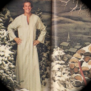 May include: A man wearing a long, striped robe with a V-neck. The robe is white and beige with vertical stripes. The man is standing in front of a snowy forest scene.