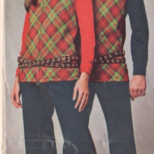 Puede incluir: Dos personas vistiendo chalecos a cuadros a juego con un patr&oacute;n rojo, verde y negro. Los chalecos tienen una cremallera y un cintur&oacute;n negro con hebillas plateadas. Las personas llevan pantalones negros y zapatos negros.