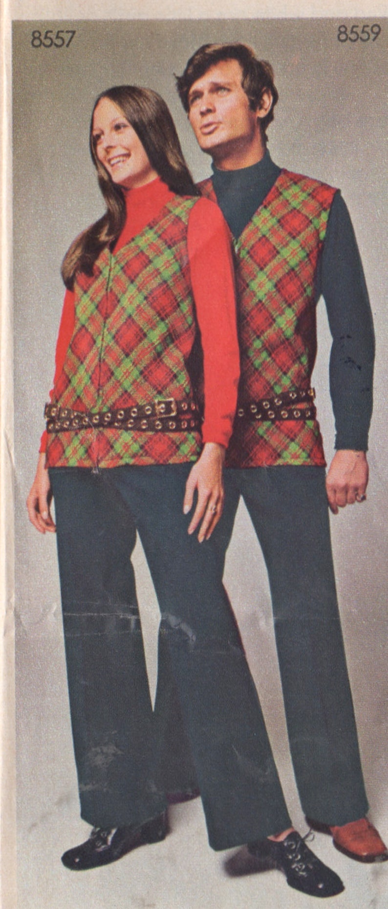 Puede incluir: Dos personas vistiendo chalecos a cuadros a juego con un patr&oacute;n rojo, verde y negro. Los chalecos tienen una cremallera y un cintur&oacute;n negro con hebillas plateadas. Las personas llevan pantalones negros y zapatos negros.
