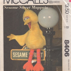 May include: A sewing pattern for making Sesame Street Muppets. The pattern features Big Bird, a yellow bird with a red beak and orange feet, standing on a street sign that reads "Sesame Street".
