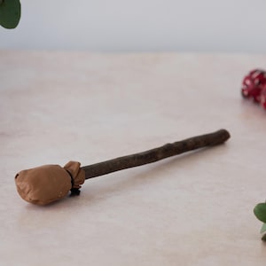 Op de afbeelding: Een bruine leren tas bevestigd aan een houten stok. De tas is met een bruin touw aan de stok gebonden.