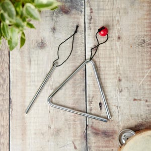 Puede incluir: Un instrumento musical de forma triangular de plata con una bola roja unida a una cuerda negra. También se incluye un palo de metal plateado.