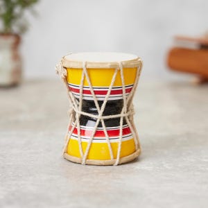 Pode incluir: Um pequeno tambor amarelo com listras vermelhas e pretas e um design de corda natural. O tambor é feito de madeira e tem uma forma redonda.