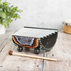 May include: A wooden xylophone with a black base and colourful painted designs. The xylophone has a curved shape and is made of metal bars. It comes with a wooden mallet.