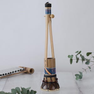 May include: A wooden musical instrument with a single string, a decorated bamboo body, and a small wooden knob at the top. The instrument is decorated with colourful dots and stripes.