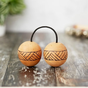 May include: Two wooden shakers with a black cord connecting them. The shakers are brown with a geometric pattern etched into the surface.