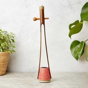 May include: A traditional Indian musical instrument called a Tanpura, made of bamboo with a red and white patterned resonator. The instrument has two strings and a wooden tuning peg.