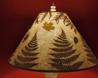 May include: A lampshade with a conical shape, featuring a beige background with a dark brown fern pattern and a few brown and yellow leaves. The lampshade has a black trim around the bottom edge.