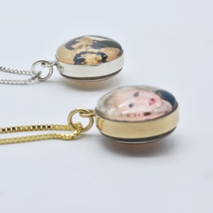 May include: Two silver and gold necklaces with round glass pendants. The pendants have photos inside. The silver necklace has a photo of a couple, and the gold necklace has a photo of a baby.