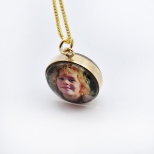 May include: A gold chain necklace with a round locket featuring a photo of a young girl with curly hair.