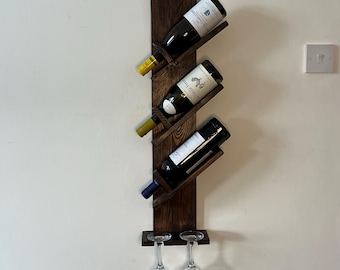 May include: A dark brown wooden wall-mounted wine rack with four slots for bottles and a shelf for two wine glasses. The rack has a staggered design with angled shelves.